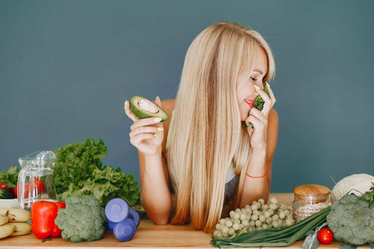 A woman with long, shiny hair surrounded by fruits and vegetables, holding an avocado, representing a hair regrowth diet plan. natural hair diet, homemade hair masks, DIY scalp care, superfoods for hair