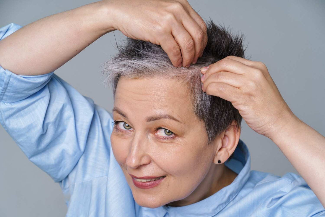 A woman examining grey hair in the mirror, highlighting common grey hair reasons. premature greying concerns, scalp health tips