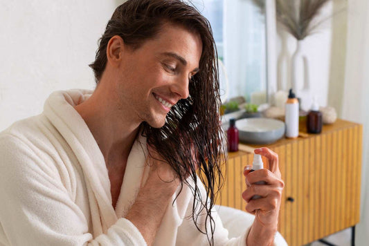 A man in a white bathrobe applying hair spray or serum to his damp hair. men’s scalp care, natural hair regrowth routine, onion oil for men, hair thickening solution, hair care spray