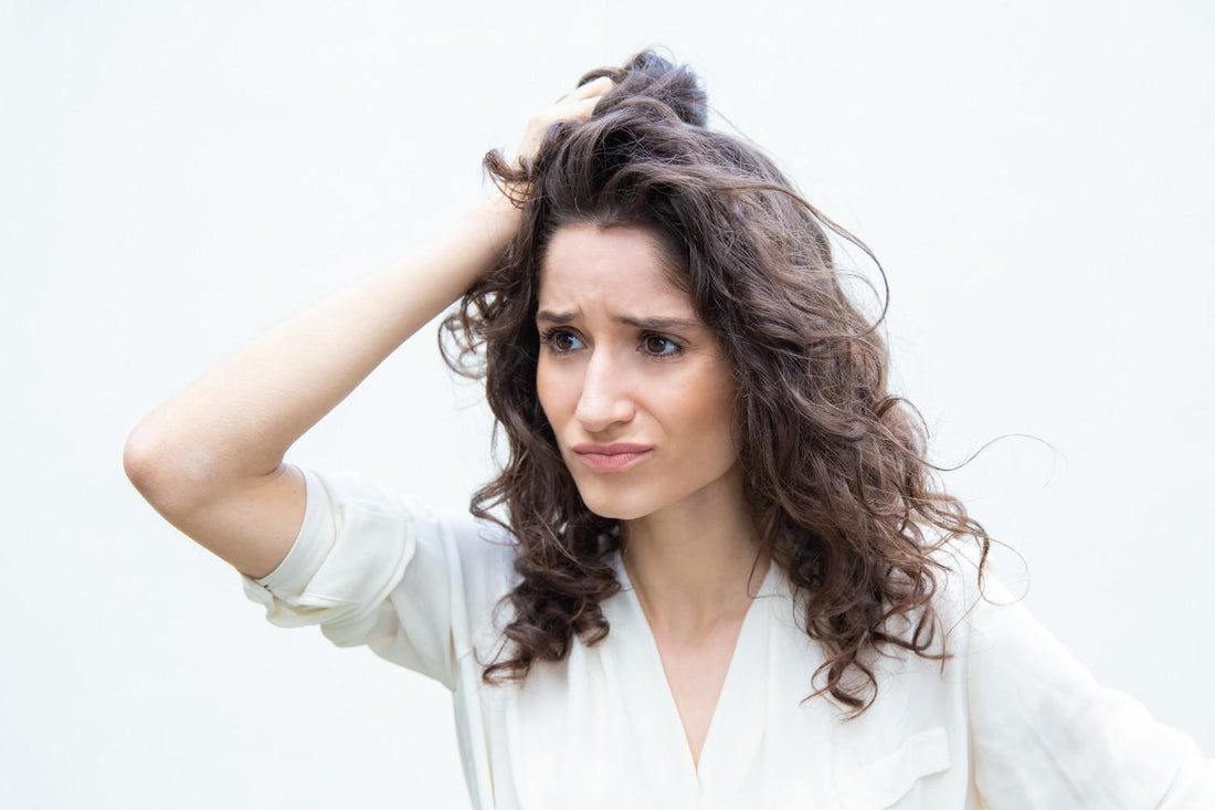 A frustrated woman touching her scalp and looking concerned, representing common hair thinning reasons in women. female hair loss stress, women hair thinning treatment, hormonal hair issues, scalp health for women, women hair regrowth solution