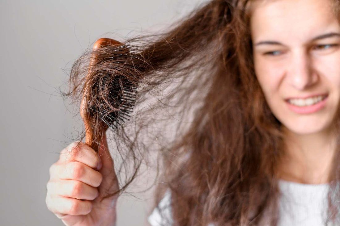 A frustrated woman looking at hair tangled in a brush, representing hair loss and damage caused by harsh shampoos and scalp irritation. hair loss and itchy scalp, anti dandruff beer shampoo