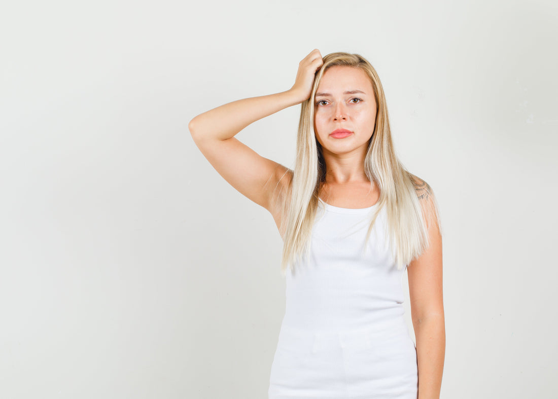 A concerned young woman in a red sweater looks at the dry and frizzy split ends of her long hair, reflecting the frustration many new mothers feel during postpartum hair loss.