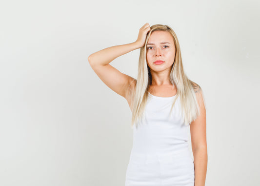 A concerned young woman in a red sweater looks at the dry and frizzy split ends of her long hair, reflecting the frustration many new mothers feel during postpartum hair loss.